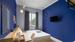 Una camera d'albergo moderna con un letto, una scrivania con un vassoio di articoli da toilette, uno specchio grande e una sveglia a muro.