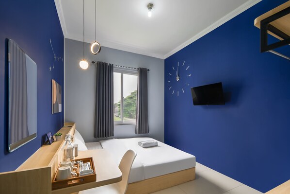 A modern hotel room with a bed, a desk with a tray of toiletries, a large mirror, and a wall clock.