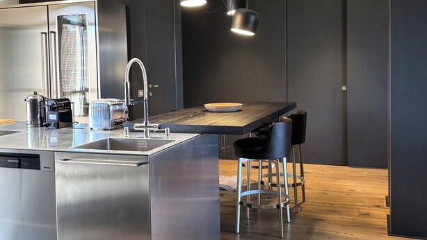 A modern kitchen with stainless steel appliances, a wooden island, and bar stools. - Exclusive penthouse with panoramic terrace and private pool in the center of Alba (ALBA)