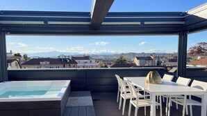 A rooftop terrace with a glass-enclosed seating area, a hot tub, and a table with chairs. - Exclusive penthouse with panoramic terrace and private pool in the center of Alba (ALBA)