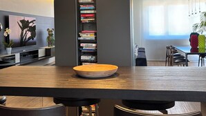 A modern dining area with a wooden table, black chairs, and pendant lighting. A bookshelf filled with books is visible in the background. - Exclusive penthouse with panoramic terrace and private pool in the center of Alba (ALBA)
