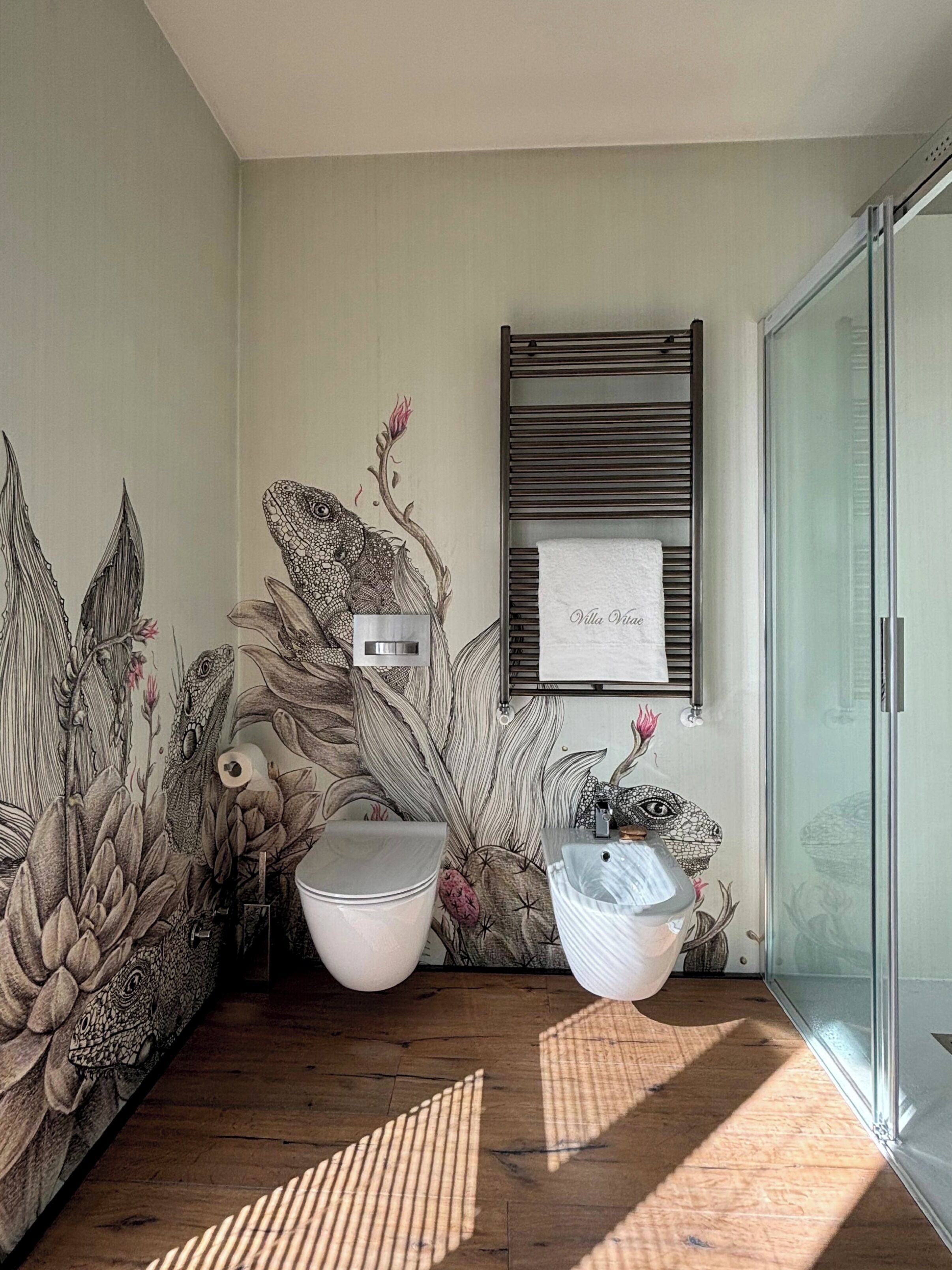 Une salle de bain ornée d’une grande fresque représentant des plantes, avec une serviette suspendue à un porte-serviettes.