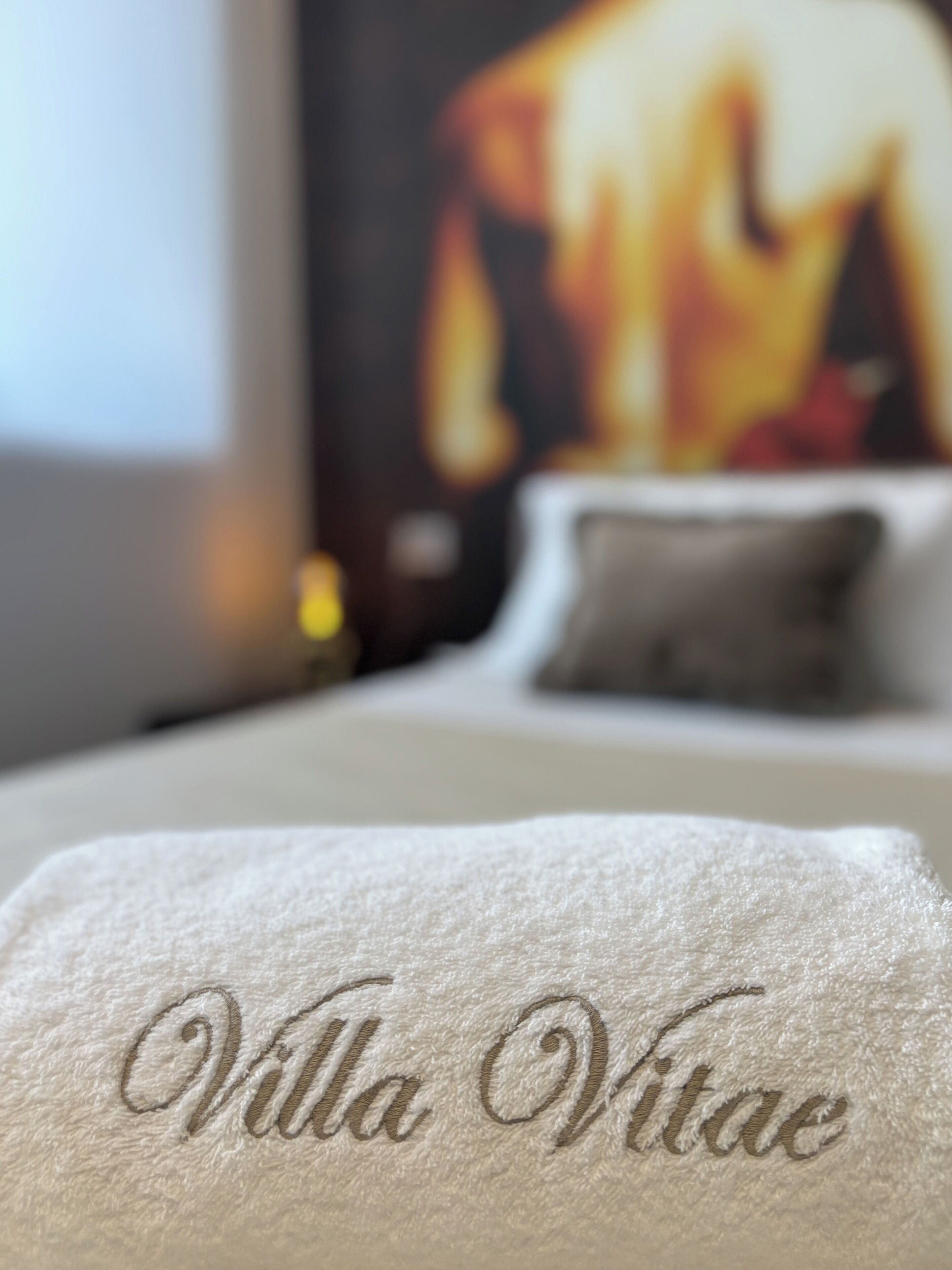 Primer plano de una toalla blanca con el texto bordado "Villa Vitae" sobre una cama.