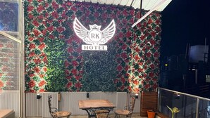 Un balcon avec un mur décoratif orné d’un logo et de l’inscription « RK HOTEL ». On y trouve une table en bois avec des chaises et un pot de fleurs.