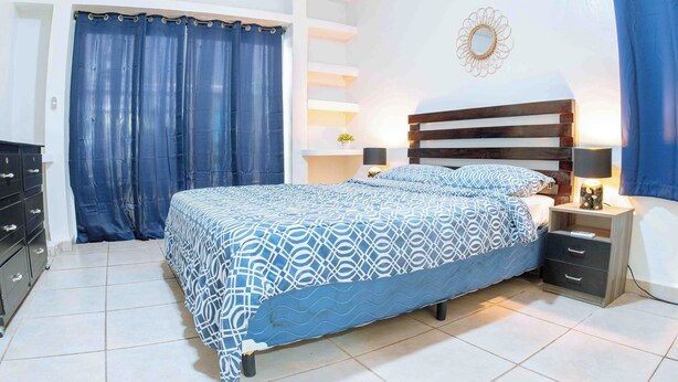 Un dormitorio con cama, mesitas de noche, cómoda y cortina.