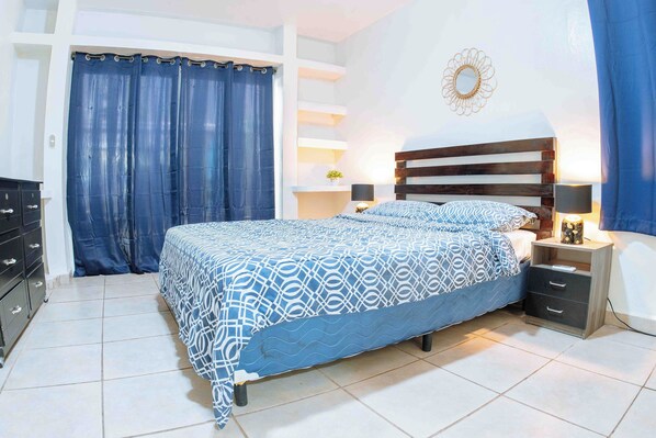 A bedroom with a bed, nightstands, a dresser, and a curtain.