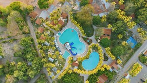 An aerial view of a resort with multiple swimming pools, palm trees, and lounge areas.