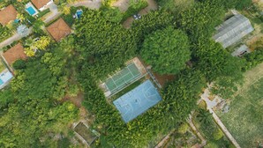 Ein Luftbild eines Wohngebiets mit einem Basketballplatz, der von dichten Bäumen umgeben ist, einem Schwimmbad und einigen Häusern.