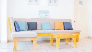 Una sala de estar moderna con un sofá color beige, cojines azules y anaranjados, y una mesa de centro de madera.