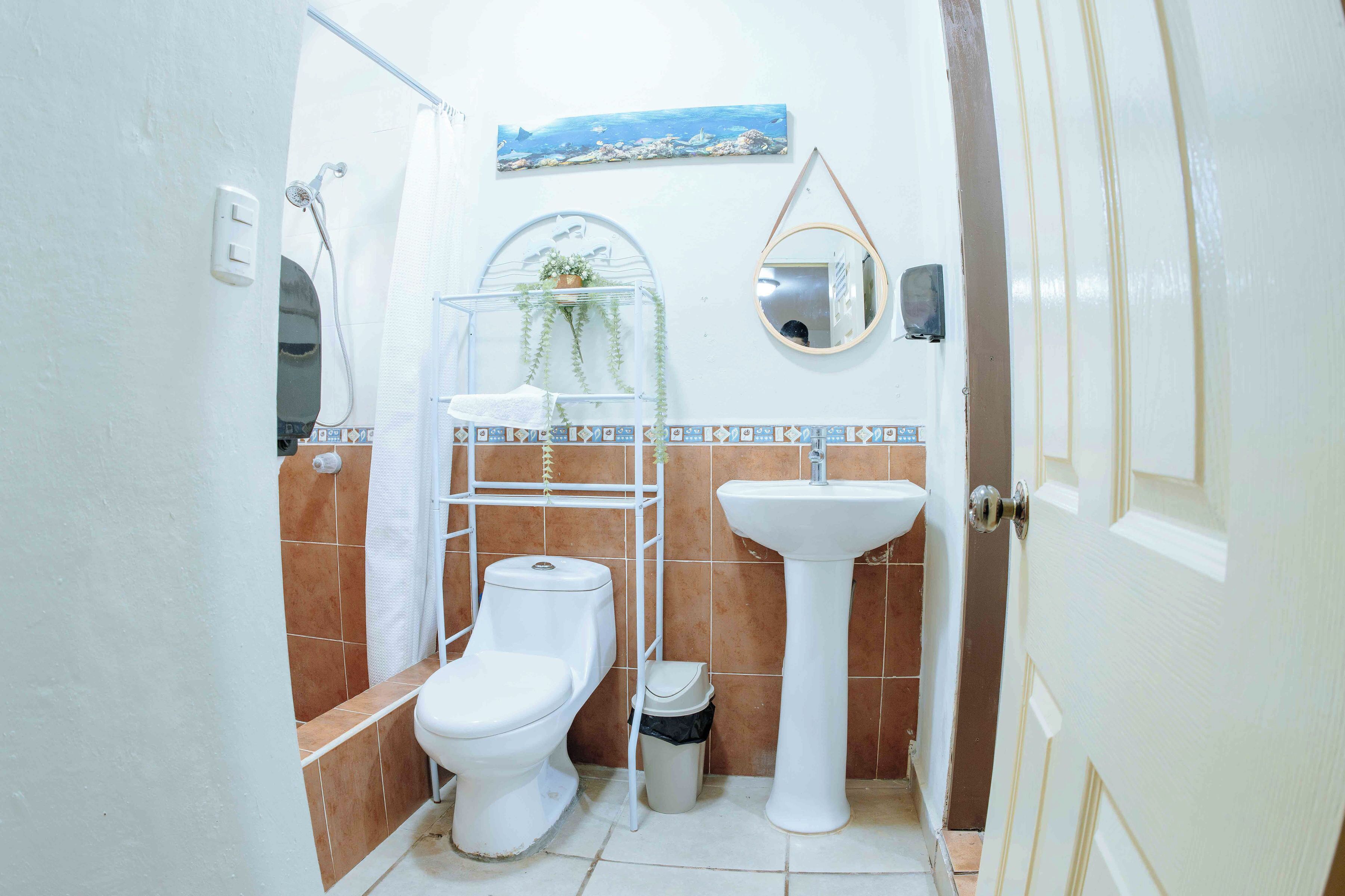 Un baño con inodoro, lavamanos, ducha y un pequeño cubo de basura.