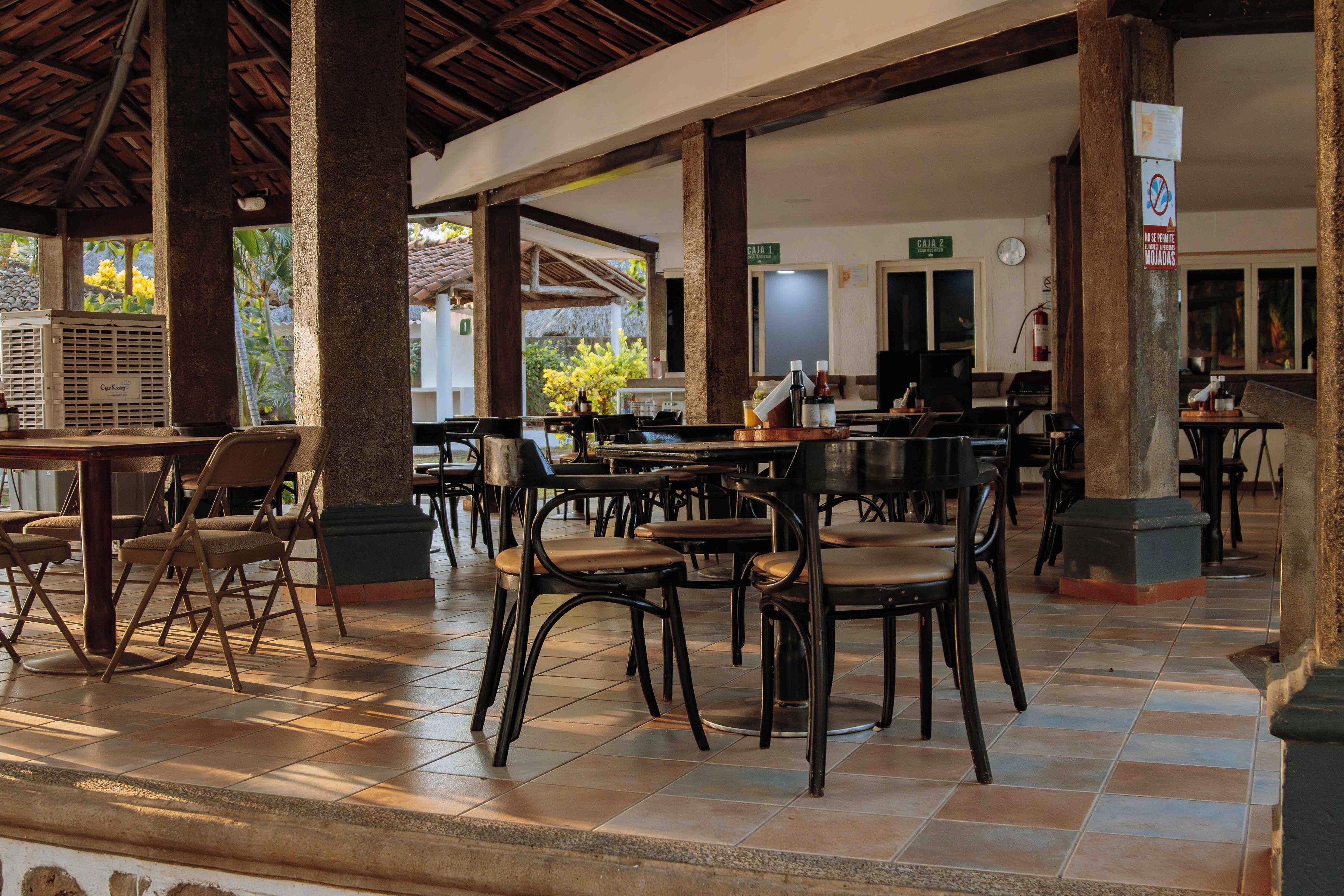 A spacious indoor dining area with multiple tables and chairs, a tiled floor, and a ceiling with wooden beams.