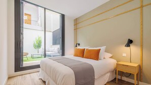 Un dormitorio con una cama grande, una mesita de noche, una lámpara y vistas a un balcón con mobiliario exterior.