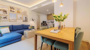 Una sala de estar moderna con un sofá azul, una mesa de comedor de madera y una cocina al fondo.