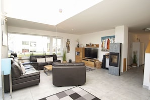 A modern living room with a sectional sofa, a flat-screen TV, a fireplace, and a large window offering a view of the outdoors.