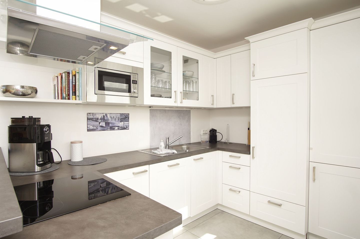 A modern kitchen with white cabinets, a built-in microwave, a coffee machine, and a glass backsplash.