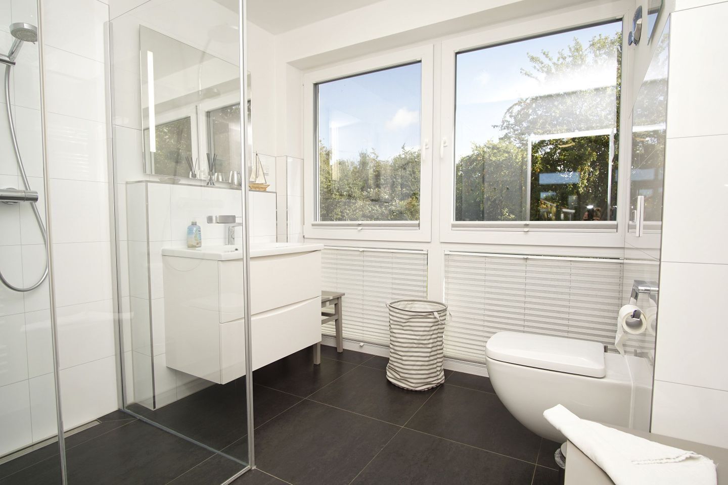 A modern bathroom with a glass shower enclosure, a white toilet, and a window providing a view of the outdoors.