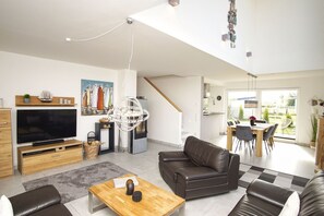 A modern living room with a flat-screen TV, leather sofa, wooden coffee table, and a dining area with a table and chairs.