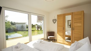 A bedroom with two beds, a wooden wardrobe, a chair, and a view of the garden. - Villa Kristall - house in an idyllic location with conservatory, terrace and garden (Trent)