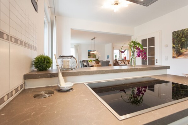 A modern kitchen with a marble countertop, a built-in stove, a small island with a plant, and a large window.