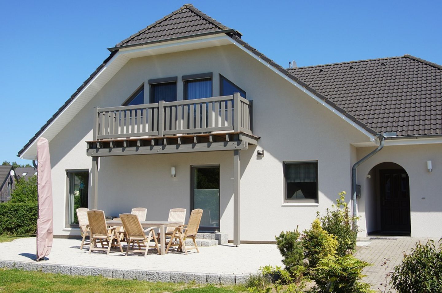 Et toetagers hus med balkon, terrasse med udemøbler og et tag med fliser.