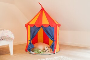 Un petit espace de jeu coloré, en forme de tente, avec un jouet en peluche à l’intérieur.