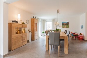 Un espace repas moderne avec une table et des chaises en bois, un coin cuisine avec des meubles en bois et une table à manger agrémentée d’un vase de fleurs.