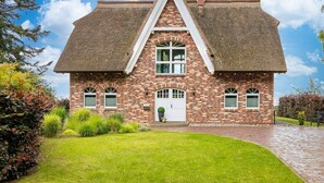 A brick house with a steeply pitched thatched roof, a central entrance with a white door, and a small front garden.