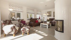 A spacious living room with floral-patterned furniture, a fireplace, and large windows with decorative shutters.