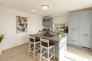 A modern kitchen with a central island, two bar stools, light blue cabinets, and a decorative wall piece.