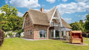 Una gran casa de ladrillo con tejado de paja, un balcón y un patio con muebles de exterior.