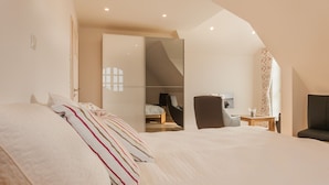 Ein modernes Schlafzimmer mit einem großen Bett, einem Sessel, einem Schreibtisch und einem Kleiderschrank.
