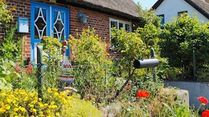 Ein traditionelles Haus mit einem Strohdach und blauer Tür, umgeben von einem Garten mit verschiedenen Pflanzen und Blumen.