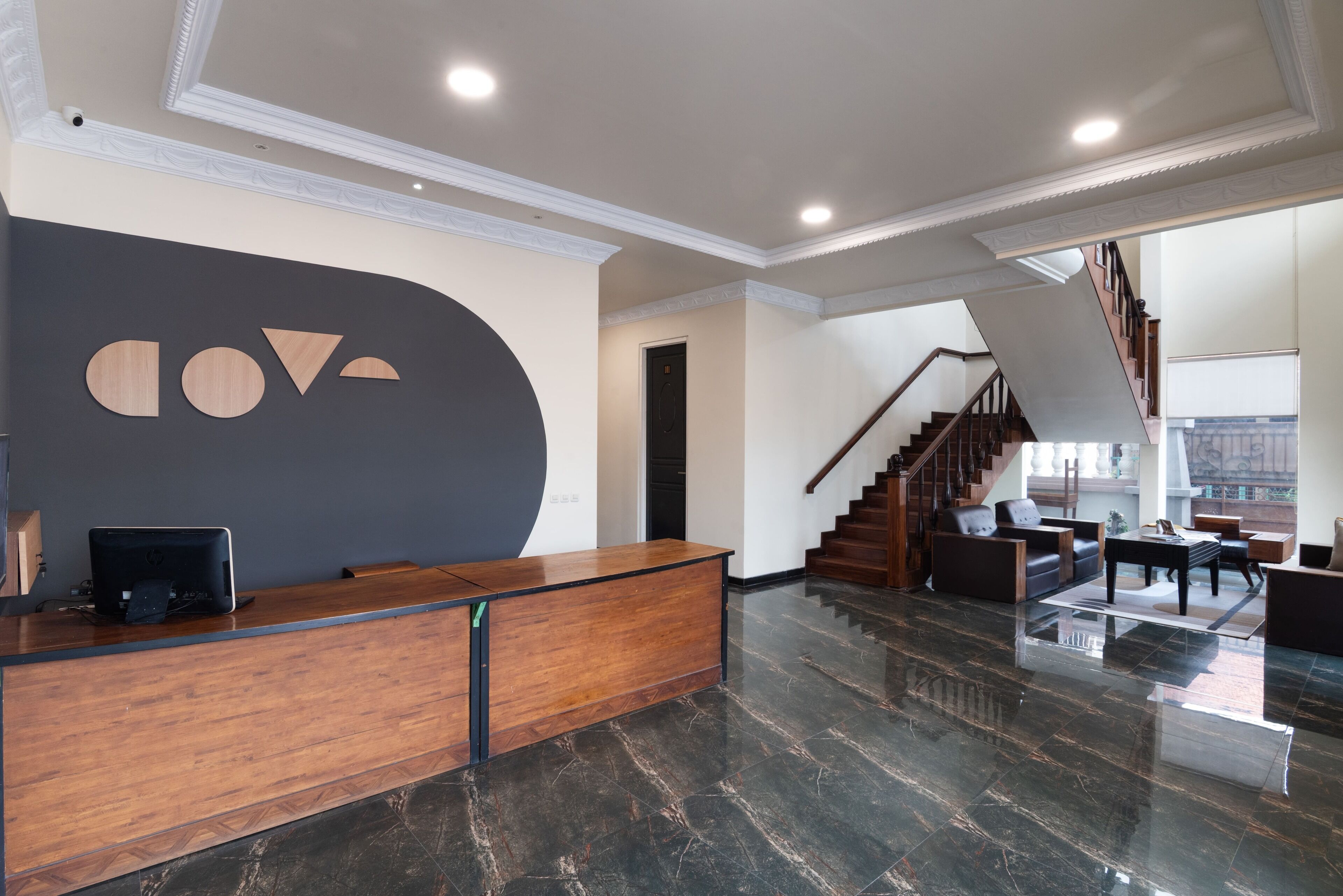 A modern reception area with a wooden desk, a large wall-mounted logo, and a staircase leading to a seating area.