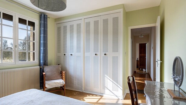A bedroom with a bed, a chair, a table with a mirror, and a set of white louvered closets. - Pavilion in the Loir Valley (Saint-Rimay)