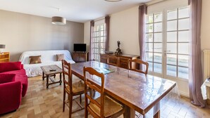 A room with a dining table, chairs, a sofa, a TV, and a window with curtains. - Pavilion in the Loir Valley (Saint-Rimay)