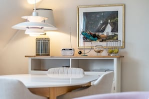 A dining area with a white table, chairs, a lamp, a radio, and a framed picture on the wall.