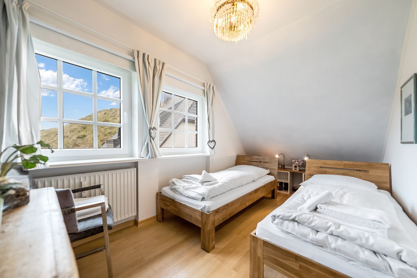 A bedroom with two wooden beds, a radiator, a desk, and a window with curtains.