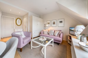 A modern living room with a purple sofa, a glass coffee table, and a white cabinet.