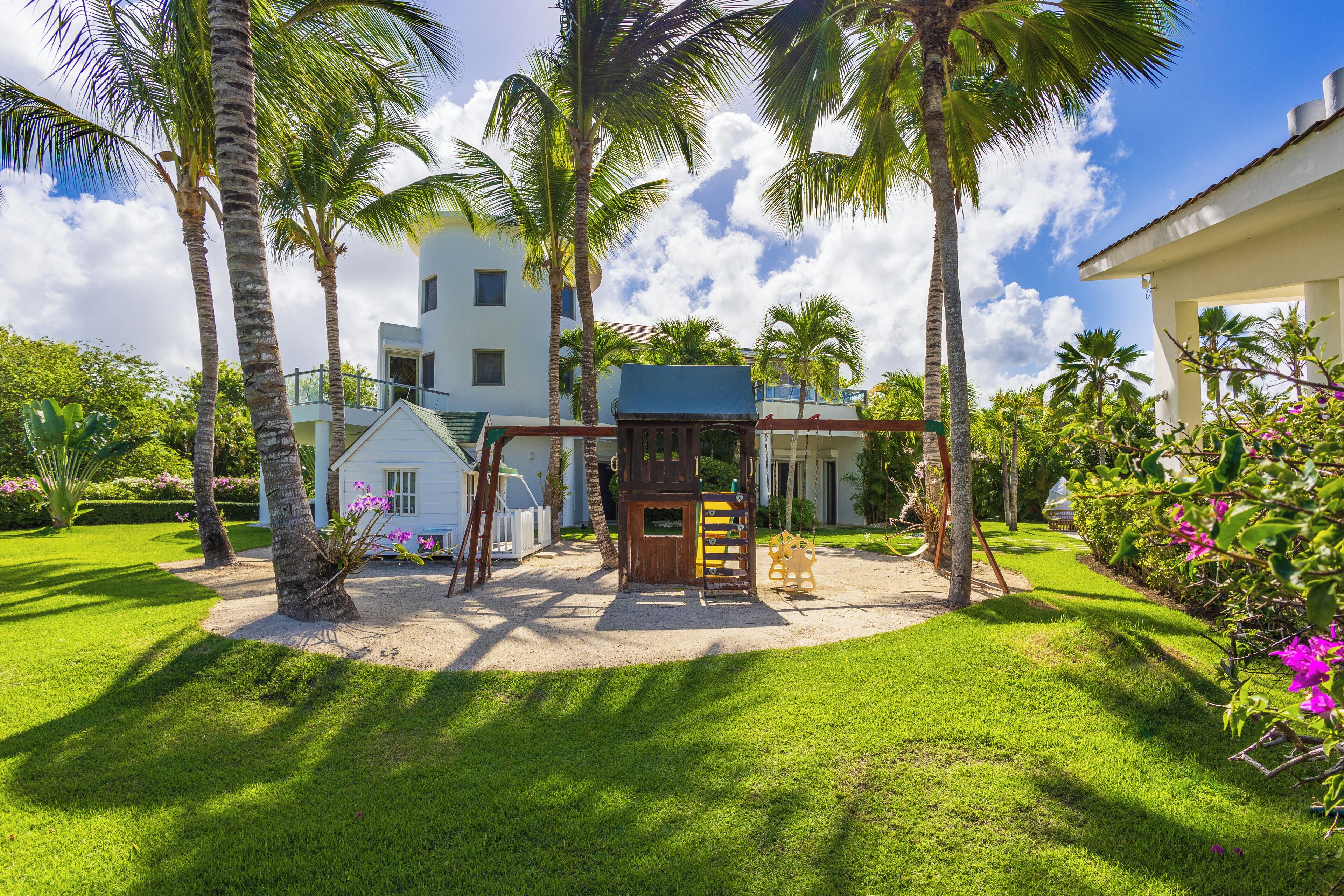 A tropical resort with a play area, palm trees, and a white building with a blue roof.