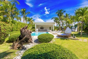 A modern resort with a pool, lounge chairs, and palm trees.