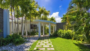 A modern building with a covered patio, surrounded by lush greenery and a stone pathway. - Villa Desiree - Family Villa in Cocotal (Punta Cana)