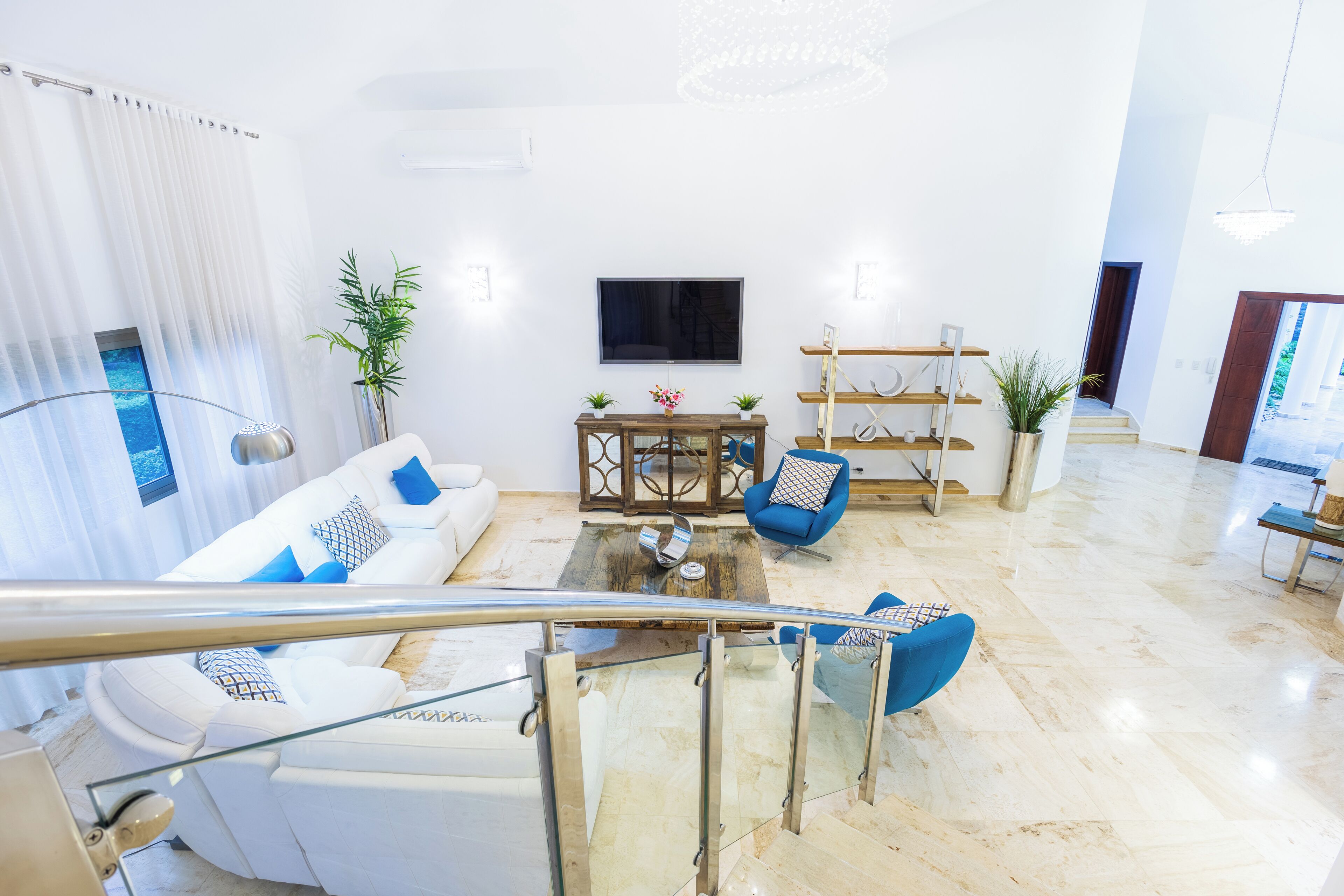 A modern living room with a white sofa, blue chairs, a coffee table, and a TV.