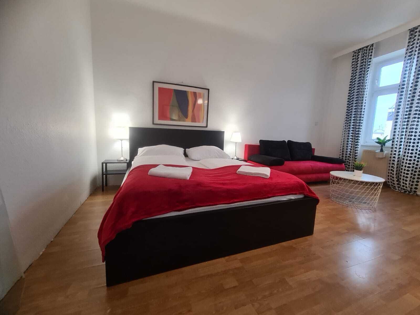 A hotel room with a large bed, a small sofa, a round side table, and a painting on the wall.