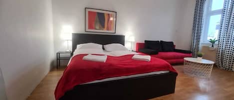 A hotel room with a large bed, a small sofa, a round side table, and a painting on the wall.