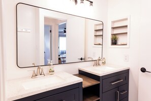 A bathroom with two sinks, a large mirror, and a wooden shelf. - Ocean+Mountain+Pool View Upgraded Condo- Steps from the beach centrally located (Kapaʻa)