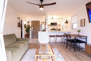 A modern living room with a sofa, coffee table, and dining area with chairs and a table. - Ocean+Mountain+Pool View Upgraded Condo- Steps from the beach centrally located (Kapaʻa)
