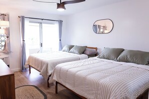 A bedroom with two beds, a ceiling fan, a mirror, and a window with curtains. - Ocean+Mountain+Pool View Upgraded Condo- Steps from the beach centrally located (Kapaʻa)