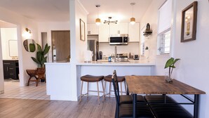 A modern kitchen with white cabinets, a wooden dining table, and bar stools. - Ocean+Mountain+Pool View Upgraded Condo- Steps from the beach centrally located (Kapaʻa)