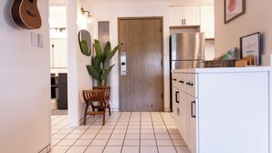 A kitchen with white cabinets, a stainless steel refrigerator, a wooden door, and a potted plant. - Ocean+Mountain+Pool View Upgraded Condo- Steps from the beach centrally located (Kapaʻa)