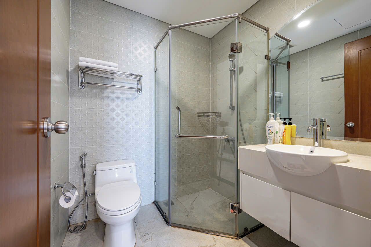 A modern bathroom with a glass-enclosed shower, a white toilet, and a vanity with a sink and mirror.
